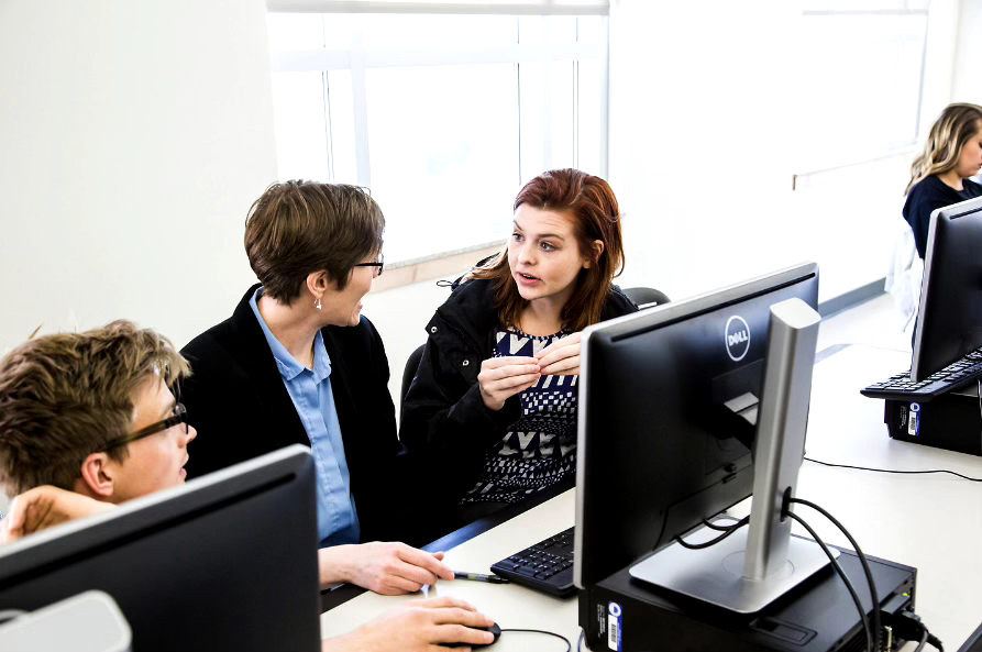 two women conversing at a desk with computer